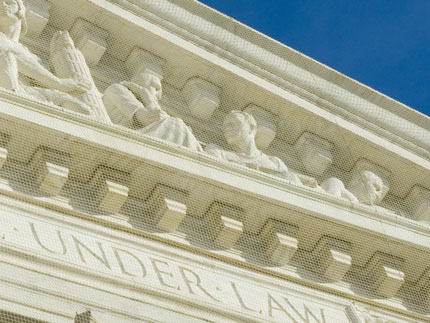 Stone relief figures above a courthouse facade with the inscription UNDER LAW